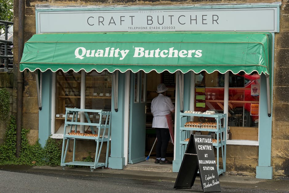The image shows the exterior of a traditional butcher shop with a light blue facade and a green awning that reads 'Quality Butchers.' Above the awning, a sign displays 'C R A F T B U T C H E R' with a